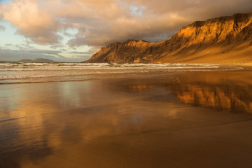 Mountains gilded by the rays of the setting sun and reflected in a wet sand on the shore of the ocean © Софья Угрик