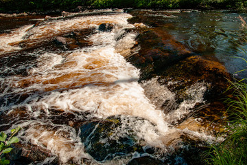 Rock under a transparent water and rapids upon it with white water