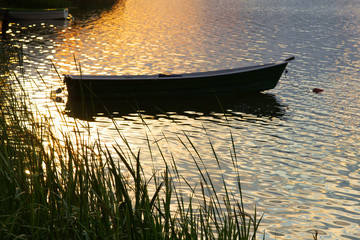 A small wooden boat on the lake in the rays of the setting sun