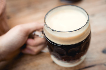 Close up top first person view photo of male holding brown black german ale czech natural glass beer cup on wooden brown tree old table. Photo in local rural pub bar Oktoberfest or event .  