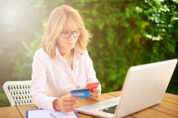 Woman using credit card and laptop at home outside on terrace. Outdoor portrait.