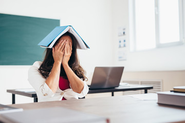 Tired female student sitting at the table with a book on her head