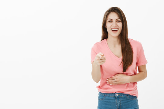 You Are Hilarious. Amused Cute European Female In Casual Outfit, Touching Belly And Pointing At Camera With Index Finger, Smiling And Laughing Out Loud, Making Fun Of Friend Or Hearing Joke