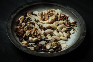 a black, rustic, wooden table stands a white plate with hand-painted black edges full of various nuts