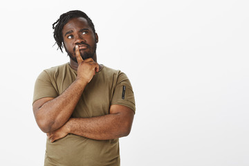 Studio shot of curious dark-skinned ordinary guy with beard in olive t-shirt, looking up and...