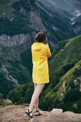 A young Girl in a yellow raincoat photographs the mountains. Georgia. Summer. August. Girl making a photo shoot of mountain. 