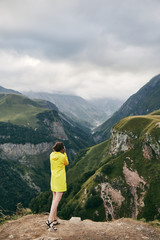 Fototapeta premium A young Girl in a yellow raincoat photographs the mountains. Georgia. Summer. August. Girl making a photo shoot of mountain. 