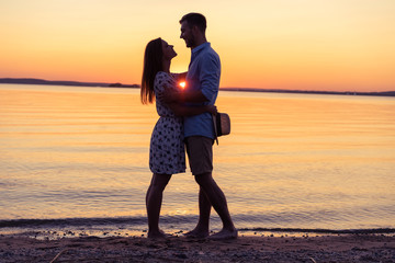 Fototapeta premium Silhouette of happy couple on beach at sunset, man taking the girl in his arms.