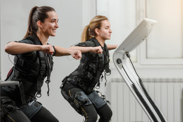 Young athletic women in EMS suits exercising in modern gym
