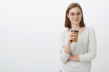 Time grab coffee to work productive. Satisfied relaxed, joyful good-looking woman in glasses and blouse holding paper cup of drink and smirking having break visiting hipster cafe over gray background