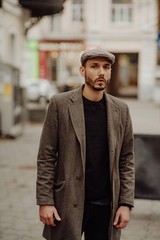 City life. Filtered effect. Stylish young American man standing on the street. Businessman wearing a grey fashionable trench coat and hat.