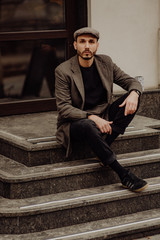 City life. Filtered effect. Stylish young American man standing on the street. Businessman wearing a grey fashionable trench coat and hat.