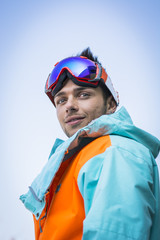 Friendly attractive skier or snowboarder against blue sky looking at camera