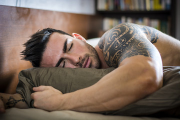 Shirtless muscular sexy male model sleeping alone on bed in his bedroom, resting