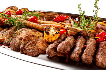 Closeup metal dish with grilled meat assortment and vegetables isolated at white background.