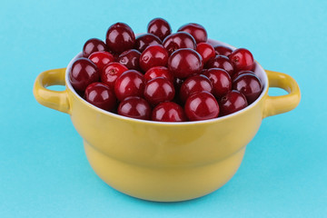 Ripe fresh bright cherries in a yellow bowl on a bright blue background