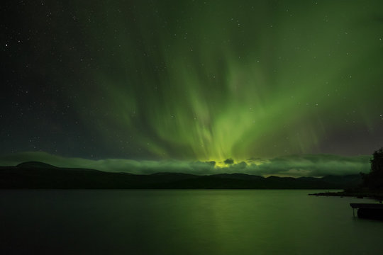 Polarlicht und Sterne &uuml;ber dem See T&auml;rnasj&ouml;n, Lappland, Schweden, gerader Horizont mit klar strukturierter Wolkendecke