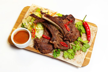 Roasted lamb meat with vegetables and sauce at wooden board with paper isolated at white background.