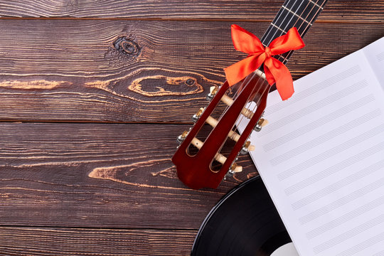 Guitar and music sheets on wooden background. Guitar handle with red bow and gramophone record with copy space. Old and modern musical equipment.