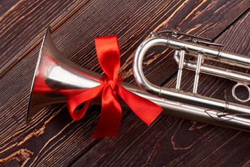 Trumpet with red bow. Shiny trumpet with red bow on brown wooden background. Instrument of jazz music.