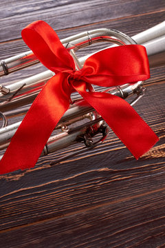 Trumpet with red bow and copy space. Classical musical instrument with red ribbon on wooden background, cropped image.