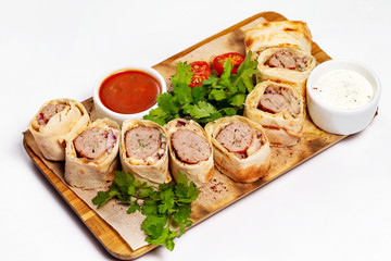 Traditional meal lula kebab - minced mutton chop slices in lavash served with sauce at wooden board isolated at white background.