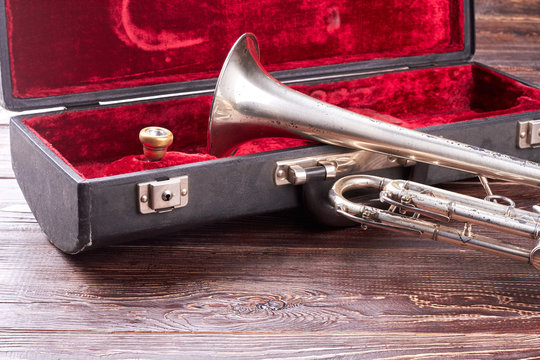 Rusty trumpet and red velvet case. Vintage trumpet instrument on wooden background. Classical jazzy equipment.
