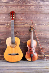 Fototapeta premium Guitar and violin on wooden background. Vintage style musical instruments on wooden surface, vertical image. Music still life.