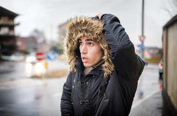 Full length of young man in coat walking under rain along the city street