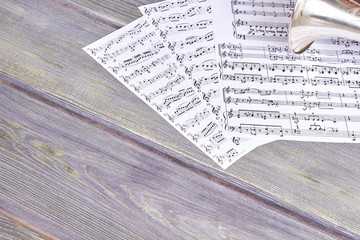 Fototapeta premium Sheets of musical notes on wooden background. Vintage trumpet on wooden background with copy space. Concept of musical education.