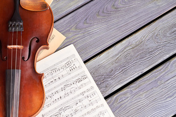 Naklejka premium Violin on old wooden boards. Sheets of musical notes and violin on wooden surface with text space. Stringed instrument of classical music.