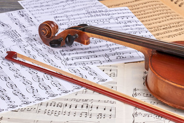 Musical background with old violin. Vintage viola and fiddle stick on musical notes sheets close up. Lesson of classical music.
