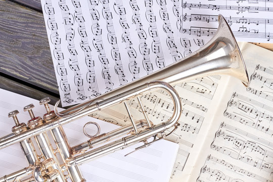 Trumpet on musical notes close up. Musical background with old trumpet and musical notes pages. Classical wind instrument.