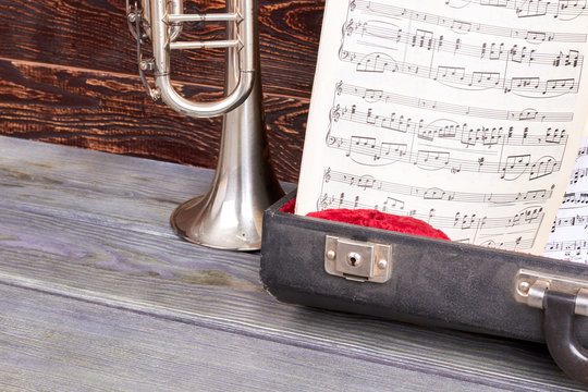 Musical notes sheets in opened case. Trumpet and musical notes on wooden background, cropped image. Retro music style.