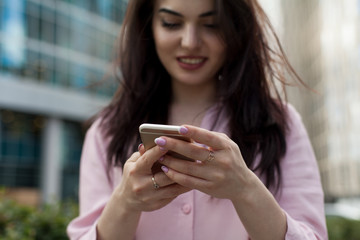 Cropped shot of young girl using modern smartphone device, female hands holding mobile phone on city street, smiling successful female entrepreneur using cellphone wireless connection for work outside
