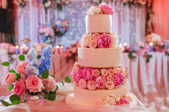 White wedding cake decorated with peony roses on pink restaurant background
