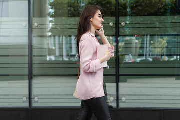 Happy successful businesswoman calling with cell telephone outside, smiling female entrepreneur managing business talking via mobile phone and walking on the city street, making phone call after job