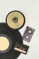 Vinyl record, compact discs and cassettes. Vinyl plate, DVD or CD disks and cassette tapes on wooden background, top view. Vintage musical devices.