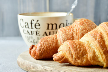 large beige Cup of coffee with milk and croissants on a wooden table. on the Cup inscription in French (top down: mocha coffee, coffee with milk, coffee without sugar)