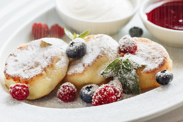 Close cheese pancakes, syrniki, curd fritters with fresh raspberries on white plate background. Decorated with powdered sugar falling down.