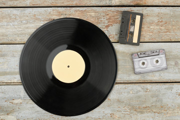 Vinyl disc and cassettes on wooden background. Black vinyl disc and cassette tapes on rustic wooden boards. Vintage musical objects.