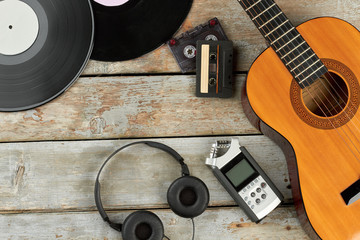 Vintage music equipment on wooden boards. Vinyl records, tape cassettes, acoustic guitar, voice recorder and modern headphones. Evolution of technologies concept.