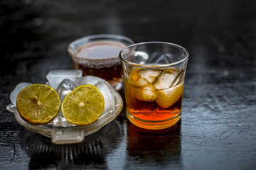 Close up of hangover remedy i.e. lemon juice and black tea in a transparent cup on wooden surface with Scotch or Scotch whiskey or Grain whiskey.
