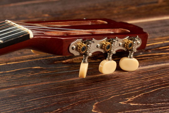 Head of acoustic guitar on wooden background. Head neck of classical guitar. Stringed musical instrument.
