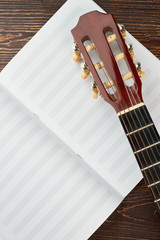 Notebook for musical notes and guitar. Top view on blank notebook for musical notes and guitar head on wooden background.