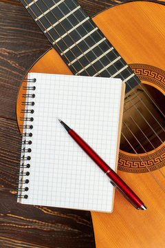 Guitar with blank notebook and pen. Classical wooden guitar with binder notepad and ballpoint pen. Workspace of musician.