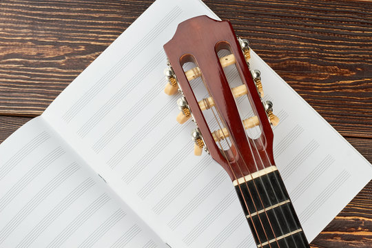 Head of guitar on musical notes. Head and pegs of a guitar on music notes book. Music sheet scores on wooden background.