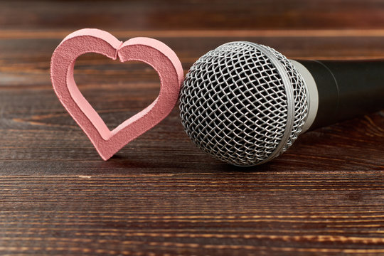 Microphone and heart on wooden background. Gray microphone and pink heart shaped decoration on brown wooden table. This is love song. For music lovers.