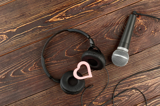Headphones and microphone on wooden background. Earphones, microphone and pink heart. Music of love.