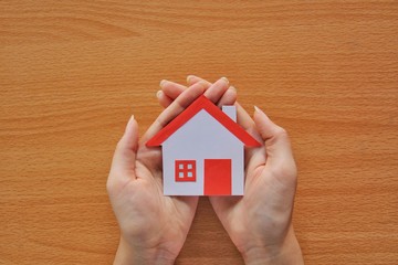 Paper red roof house in two hand on wood background,protecting home concept.